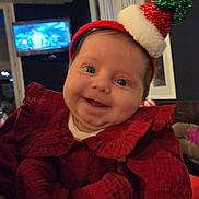 Leonor a rejoint le concours — aidez-le/la à gagner de superbes lots ! baby, celebration, child, christmas, cozy, cute, face, festive, happy, headwear, holiday_hat, indoors, infant, person, portrait, red_clothing, seasonal, smiling, television, window
