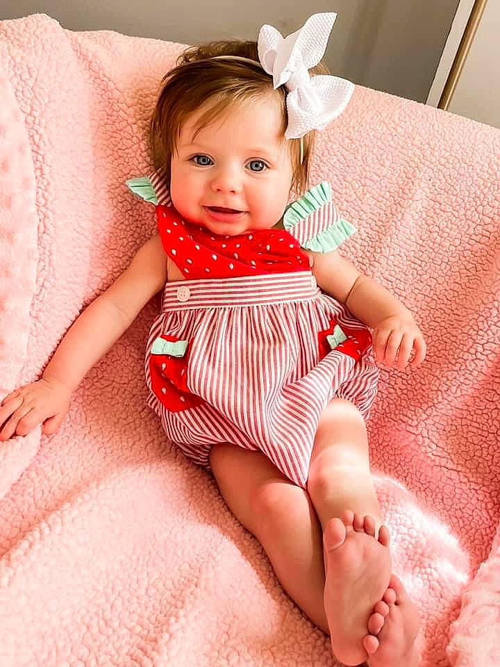 Charley is registered to the contest to win money with this photo: baby_toddler_clothing, cheek, comfort, eye, face, facial_expression, finger, head, human_body, iris, knee, neck, person, pink, skin, sleeve, smile, textile, thigh, toddler