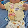 baby, infant, child, portrait, lying_down, smiling, tongue_out, cartoon_clothing, yellow_shirt, patterned_pants, winnie_the_pooh, paw_patrol, blanket, blue_background, indoor, full_body, face, hands, feet, cute