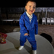 Steve joined the competition — help win amazing prizes! toddler, child, blue_suit, white_shoes, table, outdoor, night, smiling, happy, fence, chairs, stacked_chairs, formal_wear, person, standing, joyful, expression, playful, ground, party