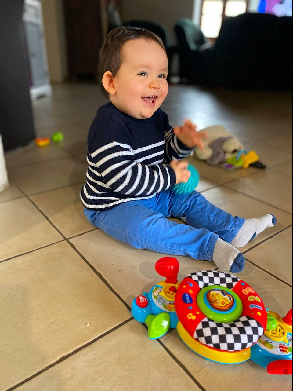 Tylio a rejoint le concours — aidez-le/la à gagner de superbes lots ! baby, baby_playing_with_toys, baby_toddler_clothing, child, floor, flooring, fun, happy, hardwood, leisure, person, play, recreation, room, sitting, smile, toddler, toy, toy_vehicle, wood