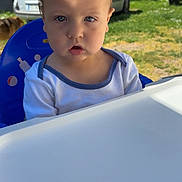 ézio participe au concours pour gagner de l'argent avec cette photo : baby, child, high_chair, outdoor, sunlight, shadow, grass, car, blue, white_clothing, face, expression, person, young_child, nature, vehicle, daylight, seat, curious, greenery