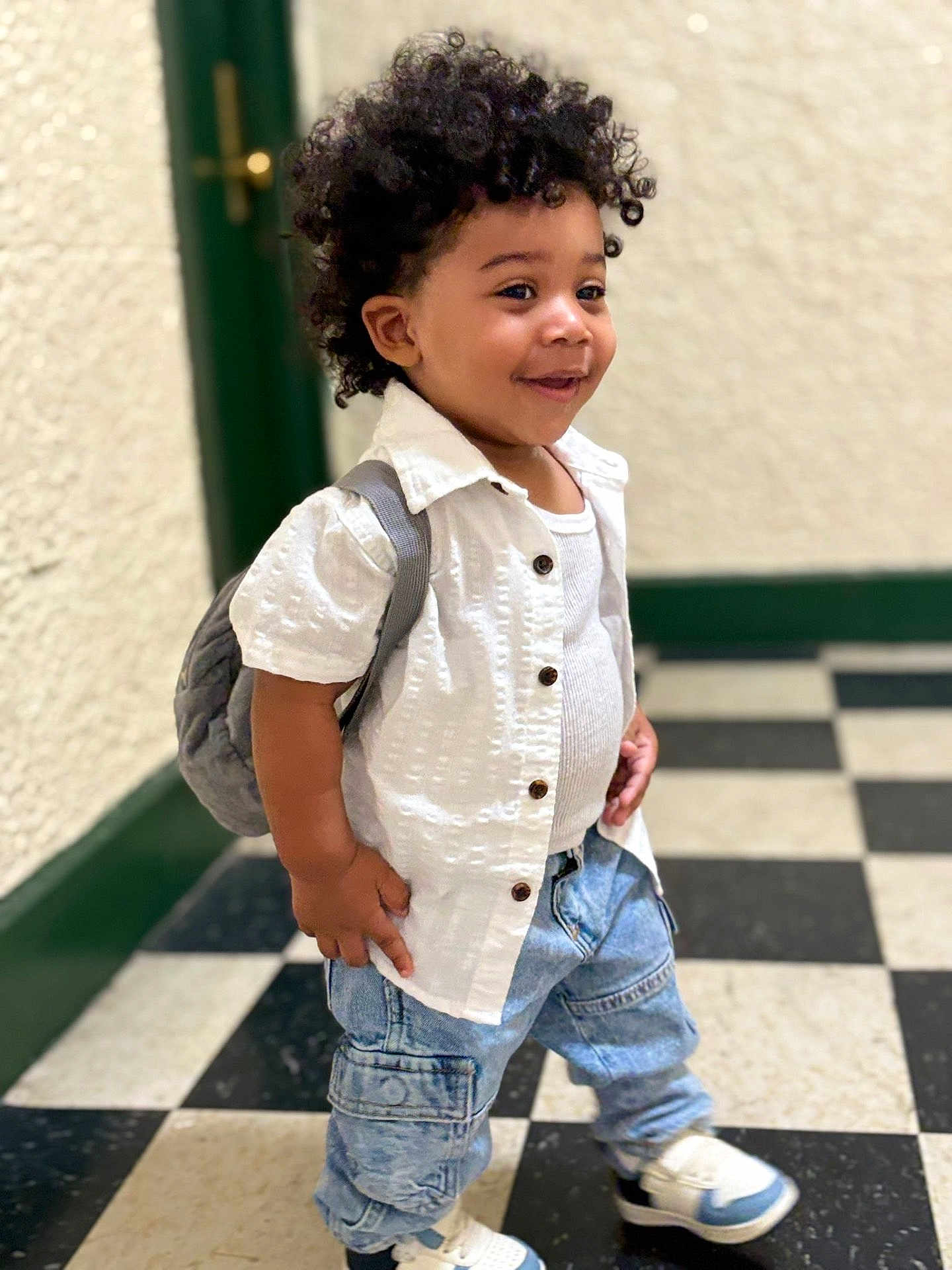 Yetxiel joined the competition — help win amazing prizes! toddler, child, curly_hair, white_shirt, denim_jeans, sneakers, backpack, smile, indoor, checkered_floor, black_and_white_floor, standing, happy, casual_clothing, person, cute, young_child, portrait, fashion, confident