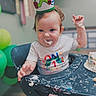 baby, birthday, cake, celebration, child, colorful, crown, face, first_birthday, food, frosting, hands, happy, high_chair, indoor, messy, party, person, shirt, smile