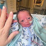 River is registered to the contest to win money with this photo: baby, infant, hospital, medical_tube, hand, adult_hand, blanket, pajamas, floral_pattern, bed, newborn, person, skin, face, eyes, hospital_room, healthcare, cute, small, reaching