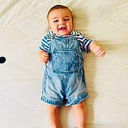 Milyann participe au concours pour gagner de l'argent avec cette photo : baby, child, denim_overalls, striped_shirt, smiling, happy, infant, bed, blanket, laying_down, cute, person, indoors, skin, foot, hand, face, head, clothing, casual