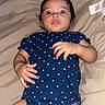 Alice is registered to the contest to win money with this photo: baby, infant, child, lying_down, bed, blanket, bedroom, portrait, face, wide_eyed, serious, polka_dot, onesie, navy_blue, hands, hair, indoor, close_up, cute, photography