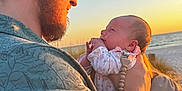 Callie is registered to the contest to win money with this photo: man, baby, beach, sunset, ocean, hat, glasses, facial_hair, holding, sky, nature, outdoor, person, clothing, love, affection, warm_light, portrait, family, happy