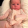 baby, infant, pink_onesie, cushion, soft_fabric, indoor, person, child, face, portrait, cute, newborn, young_child, expression, seated, relaxed, closeup, skin, head, small