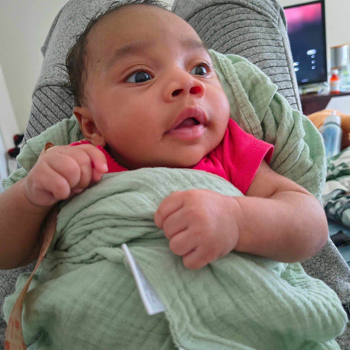 Telannie joined the competition — help win amazing prizes! baby, infant, child, portrait, close_up, wide_eyes, curious, face, hands, fists, blanket, green_blanket, pink_clothing, sitting, chair, indoor, home, television, cozy, photography
