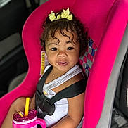 Amiri is registered to the contest to win money with this photo: toddler, child, car_seat, pink, curly_hair, yellow_bow, sippy_cup, bread, car_interior, seatbelt, happy, smiling, white_tank_top, sitting, baby, cute, food, drink, young_child, indoors