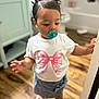 Amiri is registered to the contest to win money with this photo: toddler, child, pacifier, pink_bows, white_shirt, blue_skirt, standing, indoors, wooden_floor, door_frame, curious, hair_bows, footwear, baby, young_child, casual_clothing, person, small_child, cute, interior
