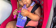Amiri joined the competition — help win amazing prizes! toddler, child, car_seat, sippy_cup, pink, unicorn, hair_buns, happy, smiling, seatbelt, clothing, legs, footwear, drink, cute, indoors, vehicle, seat, person, portrait