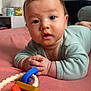 baby, infant, tummy_time, toy, rattle, bed, onesie, portrait, close_up, eyes, hands, skin, hair, cute, indoor, nursery, pink_bed, expression, playtime, child