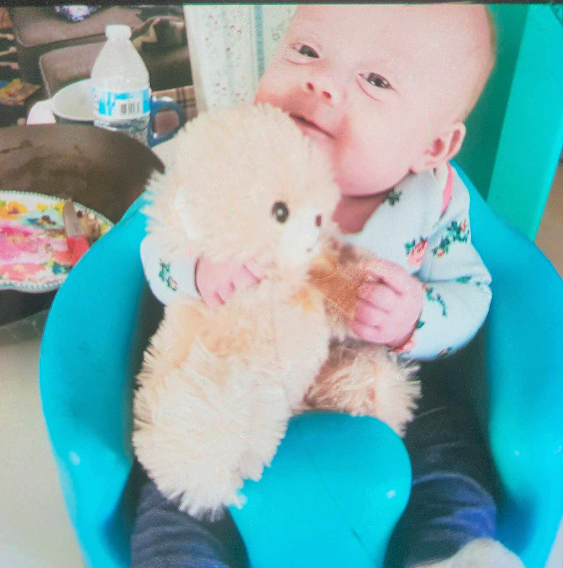Jocelyn is registered to the contest to win money with this photo: baby, teddy_bear, chair, indoor, child, toy, water_bottle, plate, clothing, person, cute, happy, smile, seated, comfort, blue, furniture, infant, cozy, casual