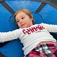 Asher is registered to the contest to win money with this photo: child, trampoline, blue, white_shirt, red_text, plaid_pants, young_child, outdoor, relaxed, lying_down, casual_clothing, portrait, smiling, happy, face, person, leisure, playtime, childhood, daylight