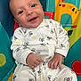 baby, smiling, infant, onesie, bee_pattern, play_mat, colorful, animal_design, cute, hands, face, happy, child, seated, indoors, clothing, person, portrait, young_child, joy