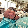 Roman is registered to the contest to win money with this photo: baby, sleeping, blanket, cozy, indoor, living_room, furniture, lamp, carpet, smile, person, infant, comfort, relaxation, home, cute, portrait, child, clothing, peaceful