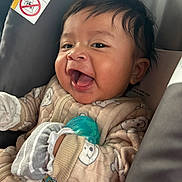 Jasiel is registered to the contest to win money with this photo: baby, infant, smiling, pajamas, mittens, car_seat, formula_bottle, happy, closeup, face, child, cute, indoor, person, infant_formula, warning_label, expression, clothing, comfort, seat