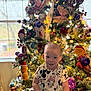 child, toddler, smiling, christmas_tree, holiday, indoor, festive, lights, ornaments, decorations, clothing, boots, table, window, happy, person, celebration, seasonal, cute, joyful