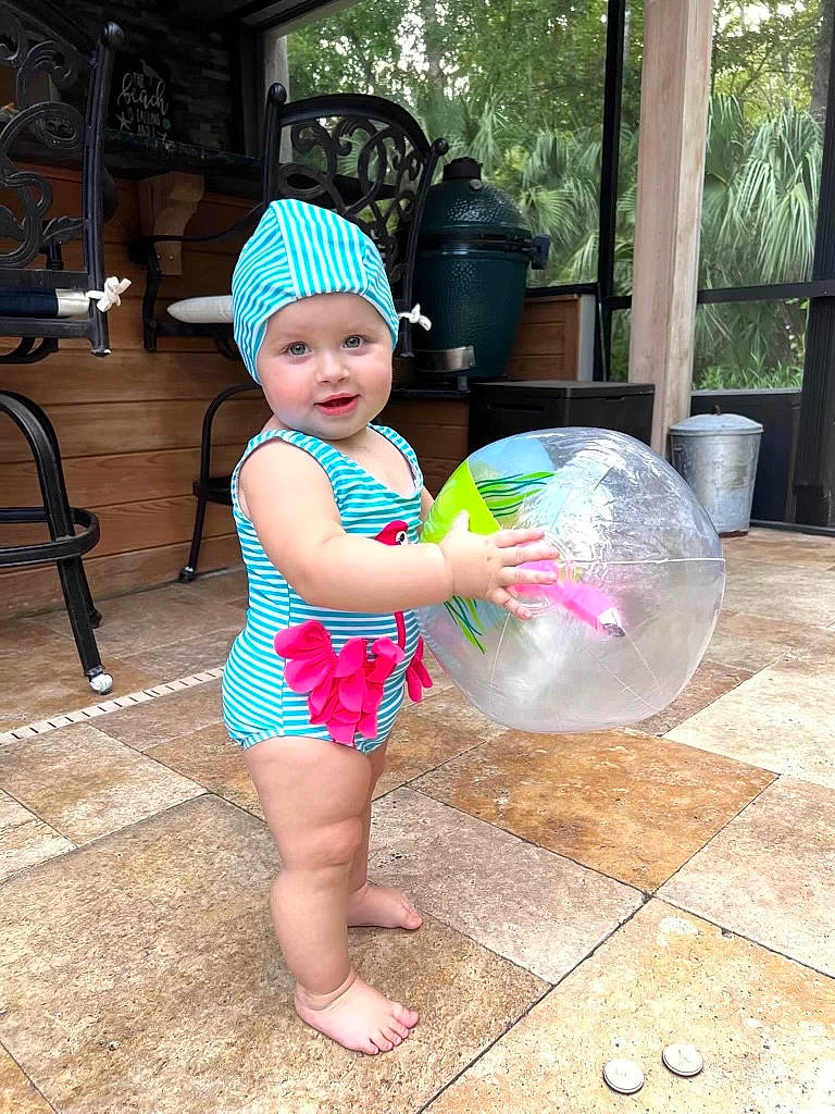 Lucy is registered to the contest to win money with this photo: baby_toddler_clothing, barefoot, child, event, foot, fun, happy, hat, headwear, leisure, party, party_supply, person, pink, plant, play, public_space, sitting, t_shirt, toddler