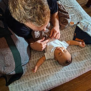 Ezra is registered to the contest to win money with this photo: baby, adult, blanket, pattern, bed, floor, hands, person, clothing, home, interaction, smile, happy, infant, wood, casual, lying_down, toddler, skin, playful