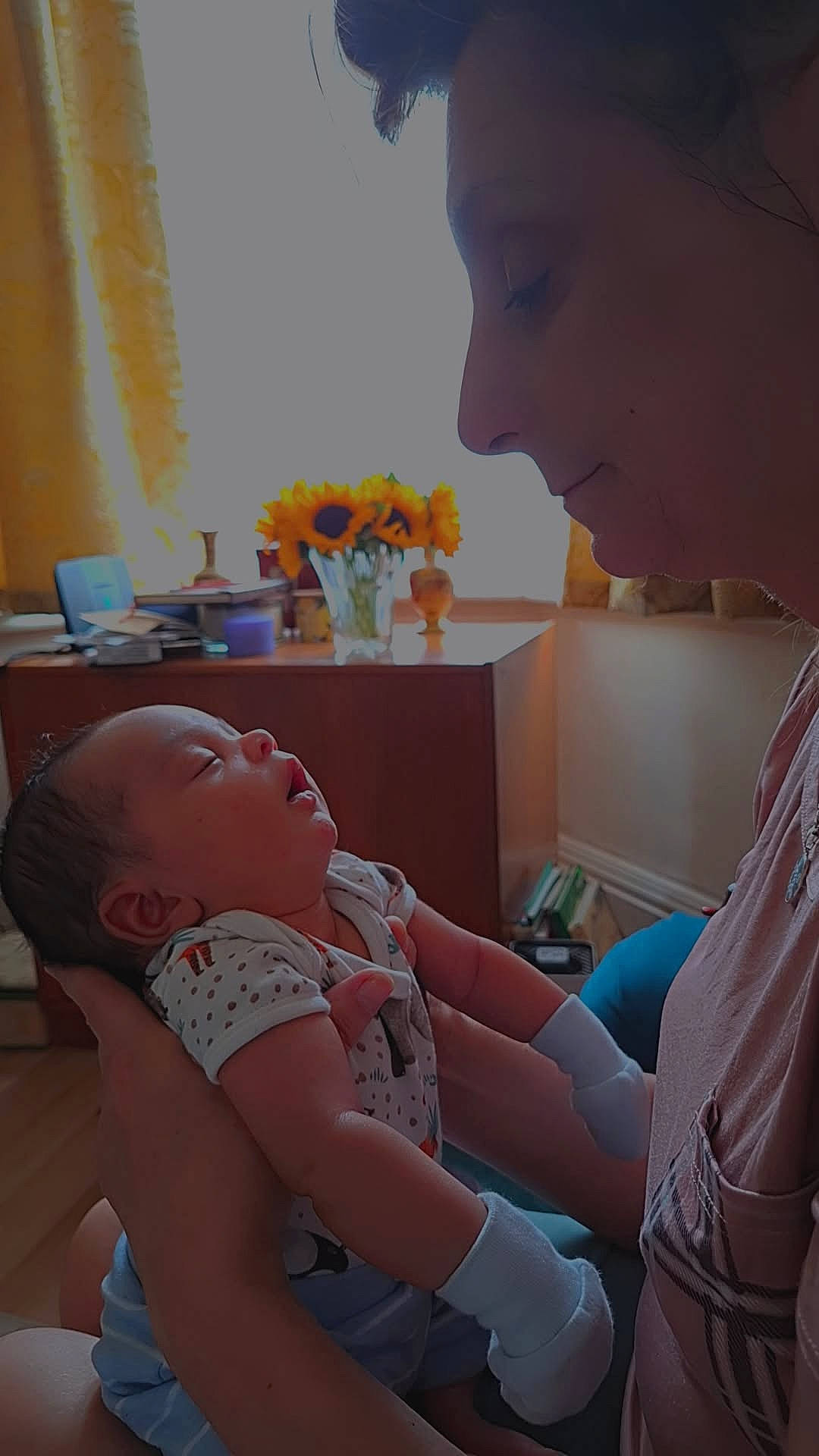 Ezra is registered to the contest to win money with this photo: adult, affection, baby, cozy, curtains, face, furniture, hand, holding, indoor, infant, love, mittens, onesie, person, portrait, profile, sleeping, sunflowers, vase