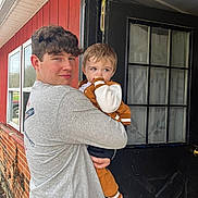 Zaydon joined the competition — help win amazing prizes! teenager, toddler, child, holding, door, window, brick_wall, black_door, casual_clothing, outdoor, portrait, person, home, curtains, smiling, face, hair, barefoot, light_grey_shirt, brown_jacket