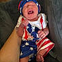 Raiden is registered to the contest to win money with this photo: baby, infant, crying, patriotic_clothing, red_white_blue, stars, stripes, hat, onesie, hand, foot, cushion, blanket, person, indoor, closeup, skin, expression, newborn, comfort