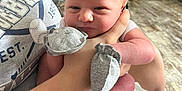 Raiden is registered to the contest to win money with this photo: baby, newborn, infant, mittens, hand, person, adult, holding, indoor, blanket, tshirt, furniture, floor, face, skin, arm, home, comfort, closeup, portrait