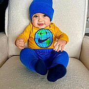 Yerick is registered to the contest to win money with this photo: baby, blue_beanie, chair, child, clothing, cute, face, feet, globe_design, hands, happy, indoor, infant, pants, portrait, seated, smiley_face, socks, soft_texture, yellow_shirt