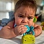 baby, infant, toy, chewing, close_up, face, hand, indoor, soft_light, expression, child, skin, young, person, play, colorful, background_blur, curtain, furniture, candid