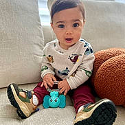 Yerick is registered to the contest to win money with this photo: toddler, child, toy, elephant_toy, sneakers, sweater, maroon_pants, couch, indoor, curious_expression, big_eyes, cute, soft_furniture, casual_clothing, handheld_toy, sitting, portrait, young_child, home, comfortable