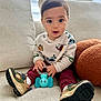 toddler, child, toy, elephant_toy, sneakers, sweater, maroon_pants, couch, indoor, curious_expression, big_eyes, cute, soft_furniture, casual_clothing, handheld_toy, sitting, portrait, young_child, home, comfortable