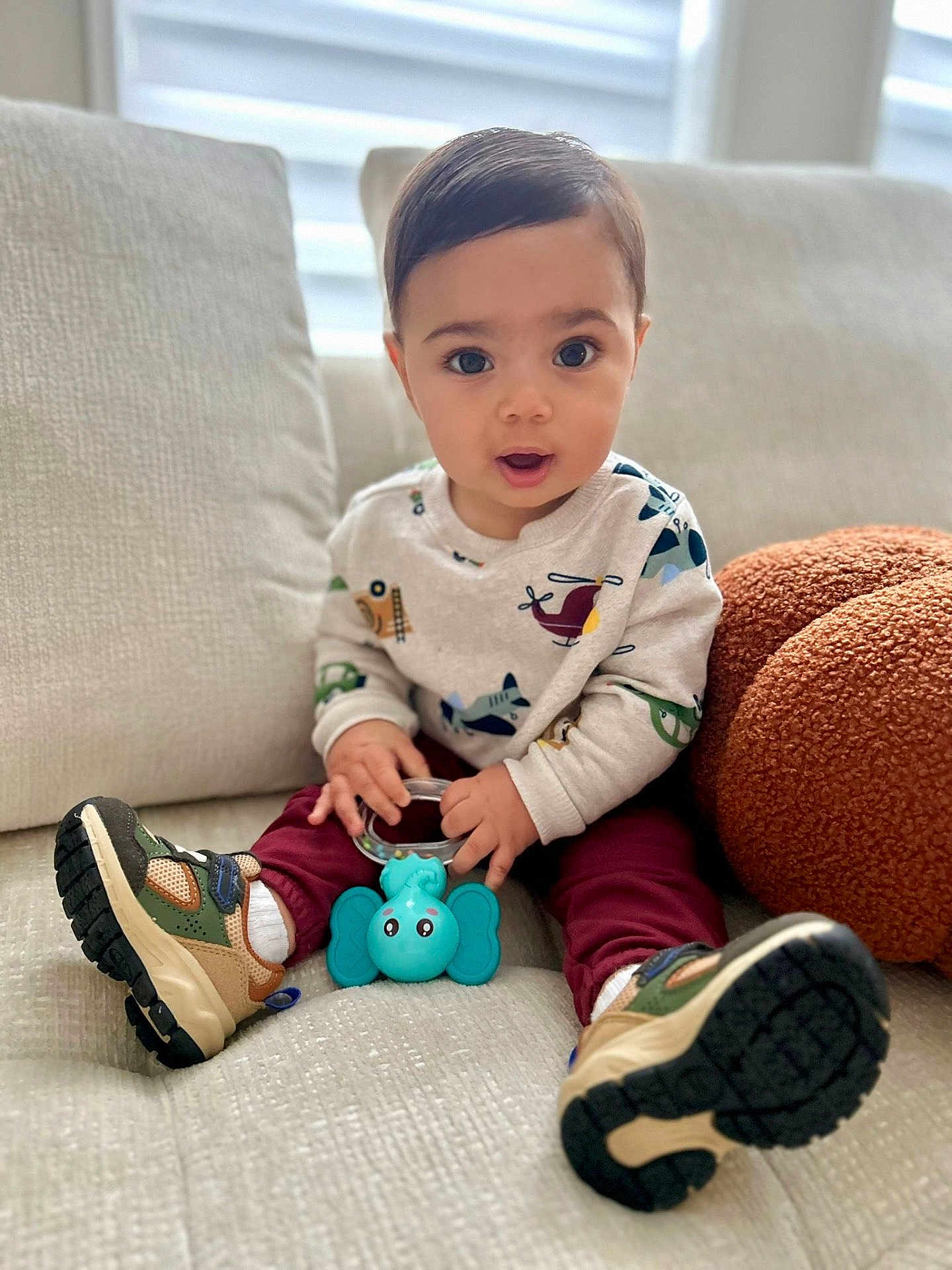 Yerick is registered to the contest to win money with this photo: toddler, child, toy, elephant_toy, sneakers, sweater, maroon_pants, couch, indoor, curious_expression, big_eyes, cute, soft_furniture, casual_clothing, handheld_toy, sitting, portrait, young_child, home, comfortable
