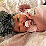Kalani is registered to the contest to win money with this photo: baby, infant, pacifier, bow, headwear, pink_clothing, blanket, soft_texture, cute, sleepwear, newborn, face, hand, lying_down, cozy, indoors, child, small_hands, expression, resting