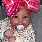 Kalani is registered to the contest to win money with this photo: baby, child, pacifier, pink_bow, onesie, floral_pattern, hands, face, cute, infant, sleepwear, soft_toy, cushion, headwear, indoors, portrait, newborn, expression, resting, closeup