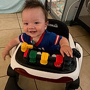 Wyatt Anthony is registered to the contest to win money with this photo: baby, child, smiling, happy, portrait, indoor, walker, activity_center, toy, infant, blue_shirt, short_sleeves, seated, playtime, tile_floor, home, furniture, baby_gear, colorful, close_up