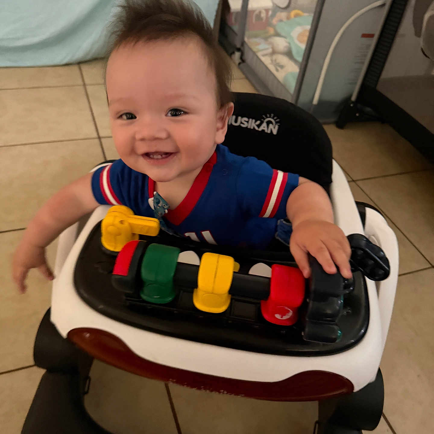 Wyatt Anthony is registered to the contest to win money with this photo: baby, child, smiling, happy, portrait, indoor, walker, activity_center, toy, infant, blue_shirt, short_sleeves, seated, playtime, tile_floor, home, furniture, baby_gear, colorful, close_up