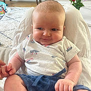 Cole joined the competition — help win amazing prizes! baby, infant, smiling, sitting, clothing, blue_shorts, patterned_shirt, person, indoor, living_room, carpet, fireplace, flower_pot, hand_holding, wood_floor, bench, cozy, cute, face, portrait