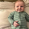baby, infant, child, smile, bed, pillow, green_onesie, striped_clothing, dinosaur_patch, comfort, indoors, portrait, cute, young_child, sleepwear, soft_fabric, relaxing, person, young_baby, lying_down