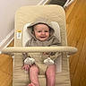 baby, hoodie, smile, infant, baby_bouncer, toy, wooden_floor, indoor, happy, child, face, barefoot, clothing, seat, home, person, young_child, cute, playful, comfort