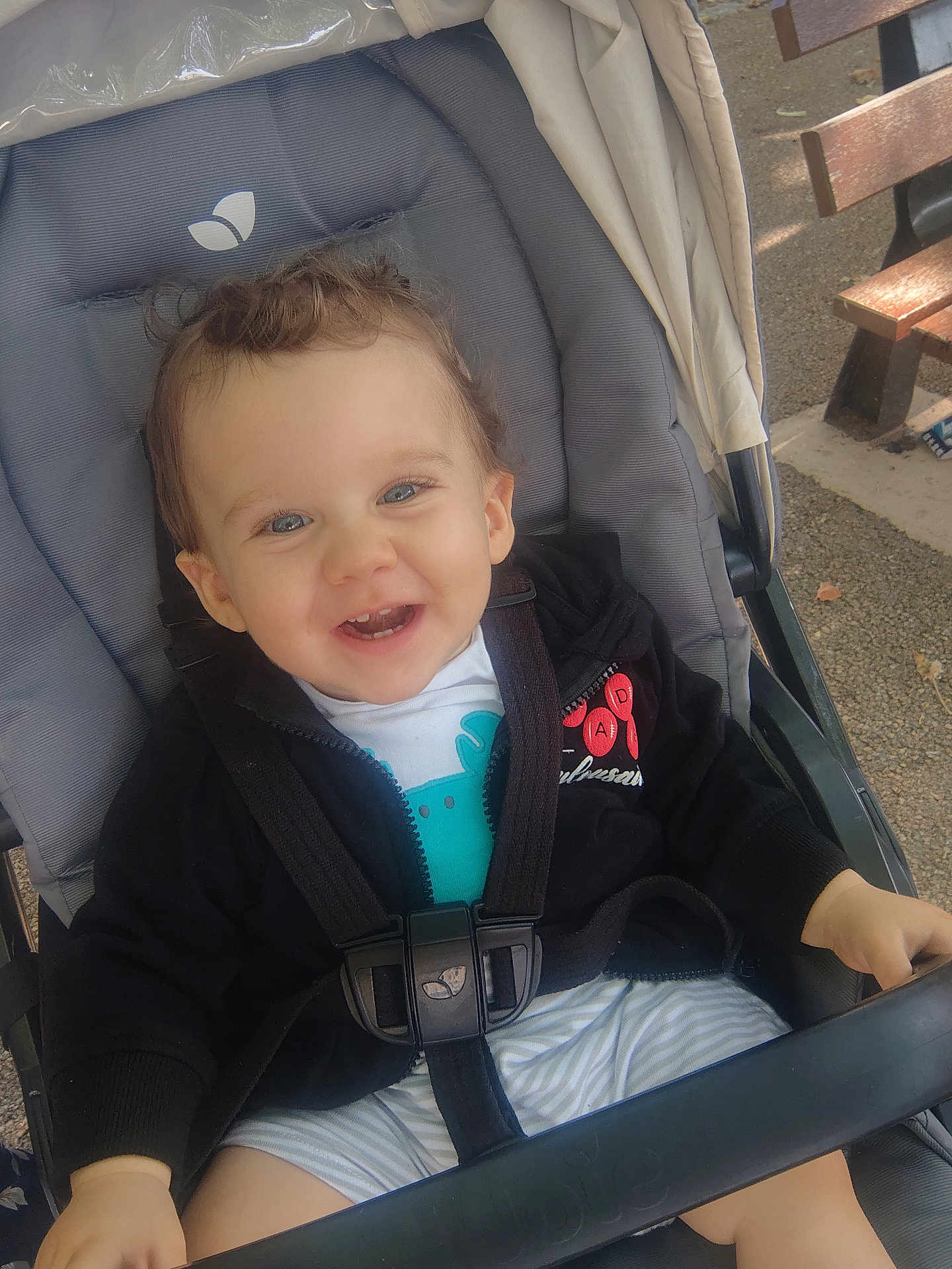 Gabin participe au concours pour gagner de l'argent avec cette photo : toddler, child, stroller, smiling, happy, outdoor, clothing, seatbelt, jacket, baby, person, face, cute, playful, sitting, daylight, bench, hair, hands, park