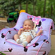 Atlas is registered to the contest to win money with this photo: baby, child, smile, purple, minnie_mouse, chair, outdoor, greenery, toy_tractor, cushion, cute, comfort, infant, clothing, socks, relaxing, portrait, nature, playful, happy