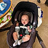 Atlas is registered to the contest to win money with this photo: baby, car_seat, stroller, bottle, indoor, floor, concrete, person, legs, shoes, carousel, colorful, expression, curious, clothing, socks, seatbelt, child, infant, baby_carrier