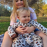 Layla joined the competition — help win amazing prizes! child, baby, outdoor, nature, grass, blanket, smiling, happy, holding, leopard_print, onesie, person, family, sibling, trees, sunlight, portrait, casual_clothing, playful, relaxing