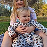 child, baby, outdoor, nature, grass, blanket, smiling, happy, holding, leopard_print, onesie, person, family, sibling, trees, sunlight, portrait, casual_clothing, playful, relaxing