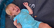 Victoria is registered to the contest to win money with this photo: child, toddler, laughing, smiling, blond_hair, blue_outfit, trampoline, outdoor, grass, garden, playground, recreation, lying_down, raised_arm, happy, portrait, closeup, daylight, leaf, playful