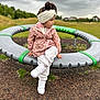 child, girl, playground, outdoor, cloudy_sky, grass, jacket, headband, white_shoes, sitting, crossed_legs, play_equipment, park, casual_clothing, nature, young_child, daytime, thoughtful, headwear, footwear