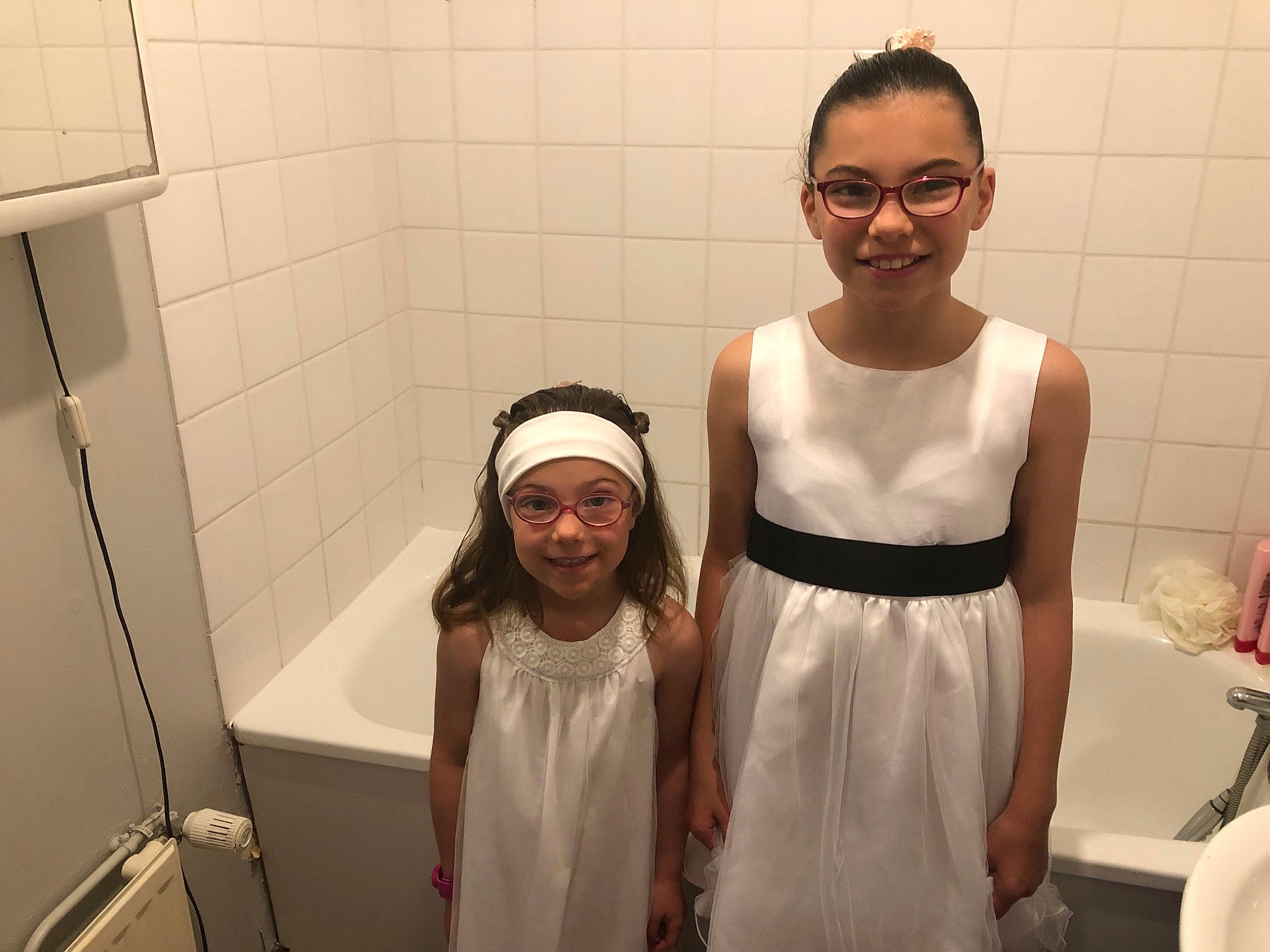 Louanne a rejoint le concours — aidez-le/la à gagner de superbes lots ! ceremony, child, dress, event, flower_girl, fun, glasses, hair_accessory, head, headwear, joy, person, plumbing_fixture, room, smile, white